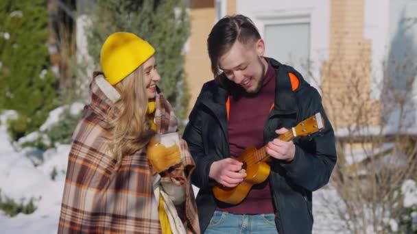 Young man playing ukulele singing serenade for smiling woman holding coffee tea cup outdoors on sunny winter day. Smiling loving Caucasian boyfriend serenading girlfriend. Music and love. — Stock Video