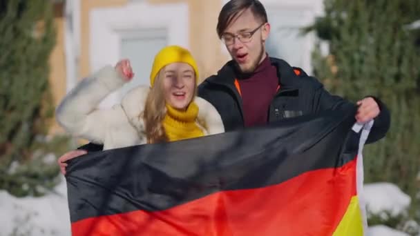 Joyful jovem casal alemão posando com bandeira nacional ao ar livre saltando sorrindo olhando para a câmera. Feliz alegre caucasiano homem e mulher regozijando lazer inverno ao ar livre no dia ensolarado. — Vídeo de Stock