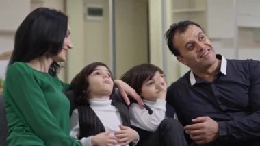 Tasasız, rahat, mutlu, çokuluslu bir ailenin hafta sonu evde televizyon izleyerek film izlemeyi tartıştığı orta boy bir fotoğraf. Gülümseyen Orta Doğulu erkek Kafkasyalı kadın ve ikiz çocuk içeride dinlenirken konuşuyor..