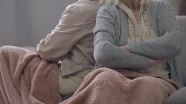 Vieille femme méconnaissable croisant les mains assis dos à dos avec un ami sur le canapé à l'intérieur. Des retraités caucasiens âgés irrités et malheureux se disputent dans le salon. Conflits et problèmes. — Video