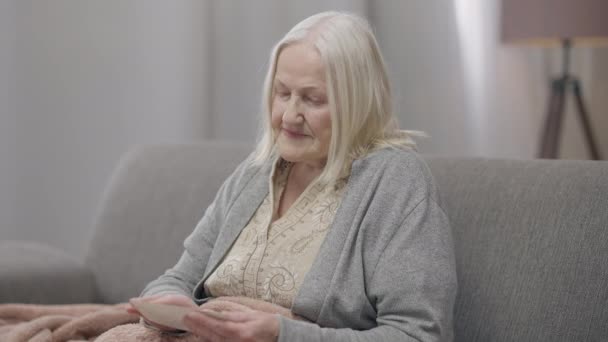 Triste donna anziana senza speranza che accarezza l'immagine in mano guardando la macchina fotografica sospirare. Ritratto di disperato depresso anziano pensionato caucasico che ricorda ricordi seduti su un accogliente divano a casa. Nostalgia. — Video Stock