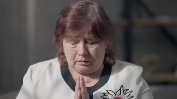 Egy közeli kép egy fehér vallásos idős nőről, aki kéz a kézben imádkozik, miközben beszél. Komoly ihletésű nyugdíjas, aki segítséget kér Istentől, hogy otthon álljon. Vallás és hit. — Stock videók