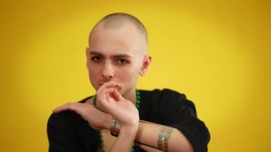 Sarı arka planda poz veren, aşırı karizmatik, siyah stil elbiseli eşcinsel erkek. Kameraya bakarak cinsiyet kimliğini ifade eden beyaz bir gencin portresi..