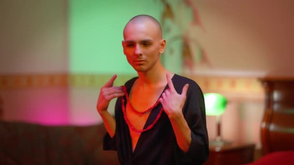 Портрет жіночого чоловіка, який намагається намисто сидіти у спальні в приміщенні. Молодий кавказький самець одягається вдома. LGBTQI fashion and style concept. — стокове відео