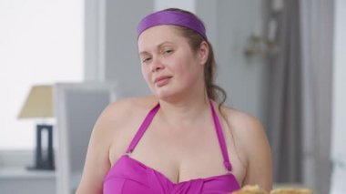 Sağlıksız hamburgerleri seçen iri yarı bir kadının portresi. Elinde sandviç ve sağlıklı sebze tabakları var. İçerde kameraya bakan kendine güvenen beyaz kadın..