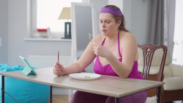 Mulher com excesso de peso deprimida olhando para fatias de pepino no suspiro prato. Retrato de frustrada senhora obesa caucasiana dieta após o treinamento em casa. Auto-controle e tristeza. — Vídeo de Stock