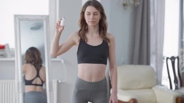 Kendine güveni tam, zayıf, ilaç şişesiyle poz veren bir kadının orta boy portresi. Kafkasyalı genç sporcu kadın ilaç desteğini elinde tutuyor ve verimliliği reddediyor..