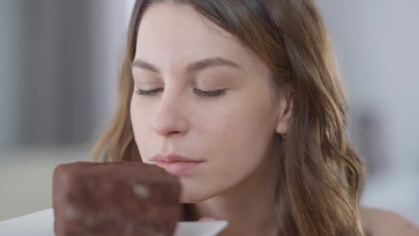 Close-up van slanke blanke jonge mooie vrouw genieten van geur van chocolade taart likken lippen. Headshot portret van prachtige brunette millennial met hazelaar ogen ruiken lekker zoet dessert. — Stockvideo