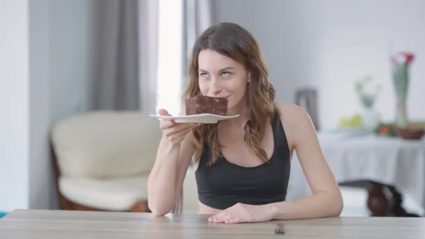 Portrait of young slim woman smelling tasty dessert breaking diet cake with satisving facial expression. Tampilan depan rata-rata dari Milenial Kaukasia menikmati pie yang tidak sehat dan lezat. — Stok Video