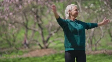 Formda gülümseyen yaşlı sporcu kadın yaz günü güneşli parkta egzersiz yapıyor. Dışarıda çalışan mutlu emeklilik eğitiminin orta boy portresi. Spor yaşam tarzı ve eğlence konsepti.
