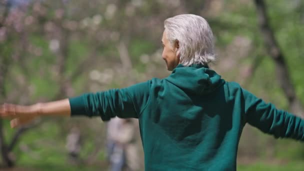 背部の後ろに手を伸ばしシニア白髪の女性のバックビュー。夏の公園で屋外でトレーニングを暖めるスリムな白人の退職者の中程度のショット。ワークアウトとライフスタイルのコンセプト. — ストック動画
