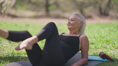 Tatmin olmuş son sınıf öğrencisi kadın bisiklet egzersizi yaparken gülümsüyor. Açık havada güneşli bir günde yaz parkında kendine güvenen zayıf, Kafkas emeklilik eğitiminin portresi. Spor konsepti.