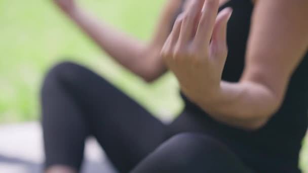 Primer plano mujer caucásica mano de yogui jubilado irreconocible ejercicio al aire libre en el parque de verano. Entrenamiento seguro de mujer en forma delgada en el día soleado sentado en la pose de loto en la esterilla de ejercicio. — Vídeos de Stock