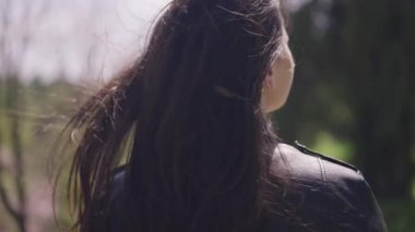 Güneşin altında duran esmer genç bir kadının arka görüntüsü. Rüzgarlı yaz gününde uzun siyah saçlar ağır çekimde sallanıyor. Kadınlık ve rahatlık kavramı.