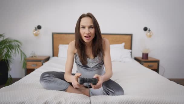 Aufgeregte schwangere schöne Frau mit Spielcontroller, die im Multiplayer-Videospiel Siegesgeste macht und in Zeitlupe lächelnd ins Bett fällt. Glücklicher Sieger jubelt über Heimerfolg. — Stockvideo