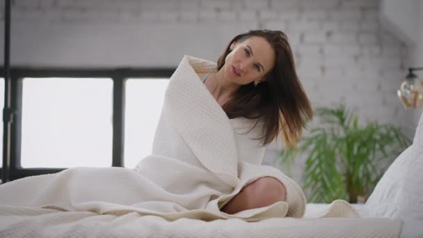 Вид спереди на прекрасную стройную белую женщину, завернутую в одеяло, сидящую на кровати по утрам и зевающую на камеру. Прекрасный уверенный молодой тысячелетие позирует в помещении дома. Медленное движение. — стоковое видео