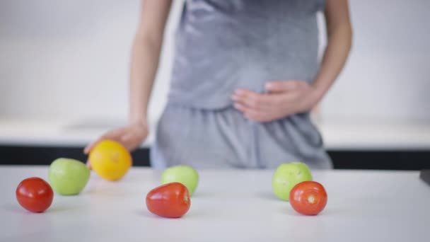 Verdure e frutta salutari distesi sul piano di lavoro con donna caucasica incinta irriconoscibile in piedi sullo sfondo. Note di alimentazione in cucina di giovane attesa. Assistenza sanitaria e gravidanza. — Video Stock