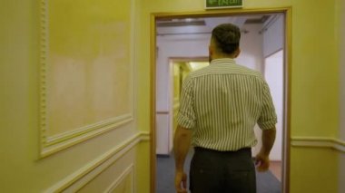 Kameralar, beyaz adamın otel koridorunda ağır çekimde yürüdüğünü gösteriyor. Kendine güvenen bir turist ya da menajerin lüks konaklama yerlerinde dolaşması. Turizm ve konfor kavramı.