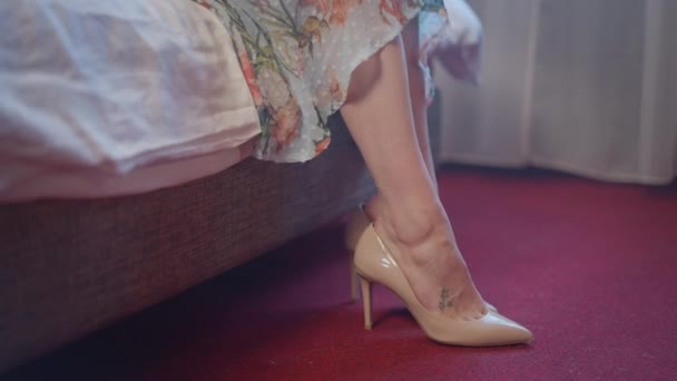 Сторонні ноги молодої кавказької жінки, які лягають на ліжко, знімають взуття з високими підборами. Невпізнавана безтурботна щаслива жінка у спальні або в готельному номері. Повільний рух. — стокове відео
