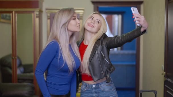 Mulheres alegres milenares tomando selfie de pé no quarto de hotel dentro de casa. Retrato de belas amigas caucasianas positivas viajando em férias no exterior. Tecnologias modernas e turismo. — Vídeo de Stock