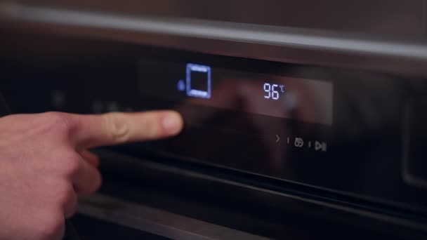 Close-up mão masculina reduzindo o calor no forno pressionando o botão touchscreen. Homem caucasiano irreconhecível ajustando a temperatura no eletrodoméstico dentro de casa. — Vídeo de Stock