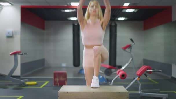 Татуированная блондинка красивая стройная белая молодая женщина, наступающая на тренажерный куб, тренирующийся в помещении. Портрет уверенной в себе спортсменки, тренирующейся в спортзале. Концепция мотивации и спорта. — стоковое видео