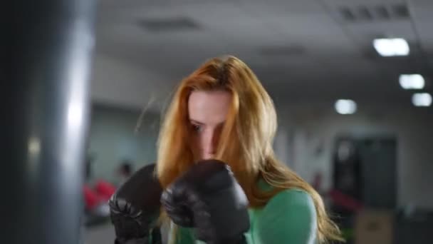 ジムでやる気のある赤毛のスポーツ女性ボクシングパンチングバッグのクローズアップ。自信を持って若い美しい白人女性のトレーニング室内のヘッドショットの肖像画。ジェンダー平等と自己防衛の概念. — ストック動画