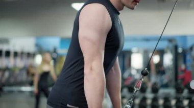 Spor salonunda el kaslarını çalıştıran tanınmayacak kadar erkeksi bir gencin yan görüntüsü. Kafkas sporcusu egzersiz makinesi çekme ekipmanlarıyla spor yapıyor. Spor konsepti.