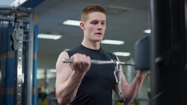 Hombre caucásico joven guapo confiado que entrena en pesas de resistencia de levantamiento del gimnasio. Retrato de deportista transpirante concentrado haciendo ejercicio en interiores utilizando la máquina de equipos. — Vídeos de Stock