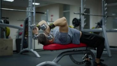 Güçlü erkeksi sporcu halterleri kaldırarak egzersiz masasında yatıyor. Konsantre olmuş Kafkasyalı esmer adam içeride spor yapıyor. Sağlıklı yaşam tarzı ve vücut geliştirme kavramı.