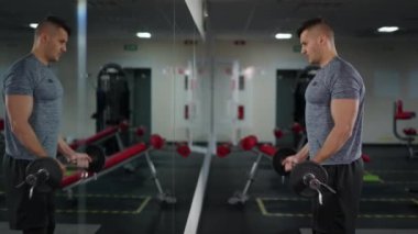 Spor salonundaki ayna yansımasına bakan erkek vücut geliştiricinin yan görünüş portresi. Güçlü kaslı, kaslı, beyaz tenli sporcu içeride antrenman yapıyor. Bpdybuilding ve özgüven.