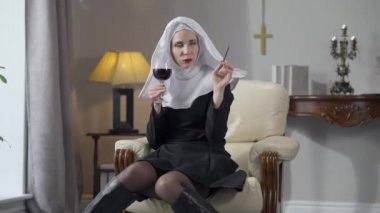 Geniş açılı beyaz kadın portresi, rahibe kostümü giymiş, elinde şarap kadehiyle oturmuş puro içiyor. Sıkıcı güzel bayan kameraya bakarak kendine güvenen yüz ifadesiyle poz veriyor.