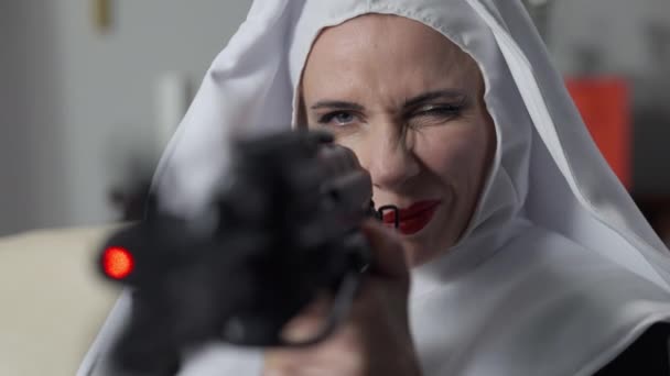 Gros plan sur le visage de la femme en costume de nonne visant avec un fusil de sniper souriant. Portrait de confiant mince belle dame caucasienne tenant arme dangereuse avec vue laser assis à l'intérieur. — Video