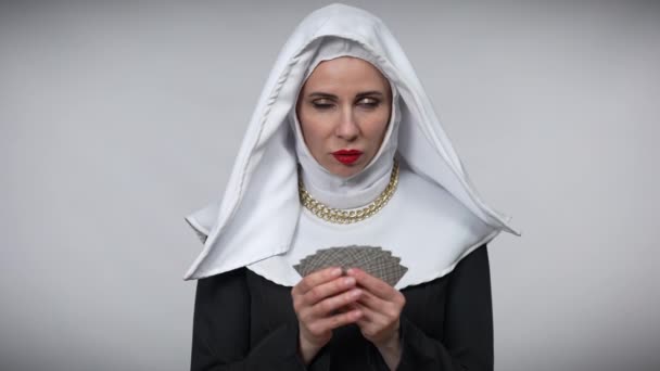 Retrato de mujer misteriosa con traje de monja sosteniendo cartas sonriendo y mirando hacia arriba. Señora caucásica confiada posando en un fondo gris. Concepto de juego y creencia. — Vídeo de stock