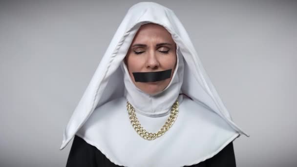 Femme désespérée désespérée en costume de nonne avec la bouche fermée avec du ruban noir tenant les mains ensemble demandant de l'aide. Portrait de triste stressé effrayé dame blanche posant à fond gris. — Video