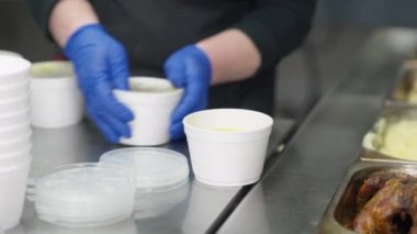 Kadın elleri, evsizler için sıcak çorbayla konteynırları kapatıyor. Ticari mutfakta çalışan ve yoksul dilenciler için yemek hazırlayan, eldivenli, tanınmayan beyaz kadın..
