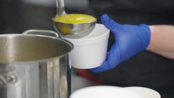 Närbild kvinnliga händer i handskar hälla soppa i engångs matbehållare. Oigenkännlig vit kvinna förbereder ta bort order för klient i cafeteria inomhus. — Stockvideo