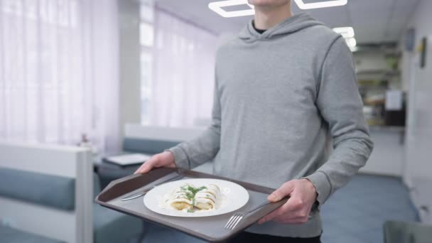 Nierozpoznawalny student trzymający tacę ze słodkim widelcem do naleśników i nożem stojącym w stołówce. młody biały mężczyzna pozowanie z pyszne jedzenie w stołówce. — Wideo stockowe