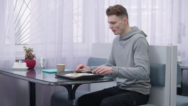 Occupato a correre giovane studente maschio mangiare frittelle bere caffè e lasciare mensa con tablet. Ritratto di un bel caucasico sicuro di sé che si allontana dalla caffetteria dopo la pausa pranzo. — Video Stock