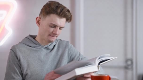 Portré a lefoglalt kaukázusi fiatalemberről, aki könyvet olvas a kávézóban. Boldog elmerült férfi olvasó élvezi hobbi ebédszünetben a diák kulacsban. Intelligencia és oktatás. — Stock videók