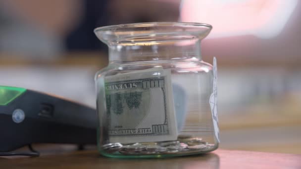 Primer plano consejos tarro con mano caucásica femenina poner dinero en efectivo en el interior. Visitante irreconocible café dejando dinero para consejos en la cafetería en el interior. — Vídeo de stock