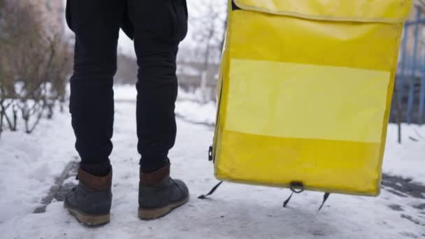 Nerozpoznatelný muž dává žlutý termální sáček na zimní chodník a odchází. Mladý kavkazský kurýr opouští odvětví doručovacích služeb. — Stock video