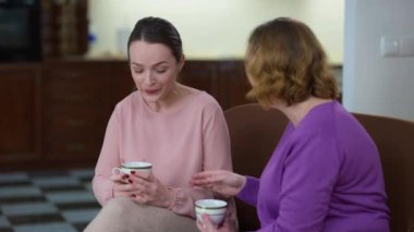 Annesinin konuşmasını dinlerken gülen sevimli genç bir kadın. Rahatlamış mutlu beyaz kızın portresi. Yetişkin ebeveynlerle evde çay içerek hafta sonunun tadını çıkarıyor..