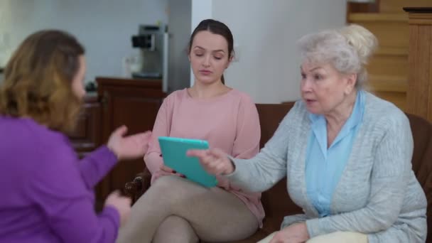 Retrato de una joven hermosa mujer delgada navegando por las redes sociales en la tableta ignorando la discusión familiar en el frente. Desinteresado caucásico millennial dama en casa con enojado madre y abuela peleando. — Vídeos de Stock