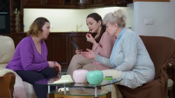 Wide shot of slim beautiful millennial woman applying lipstick as mother and grandmother giving advices talking and gesturing. Portrait of confident Caucasian lady getting ready for a date at home. — Stock Video