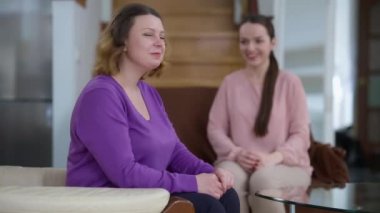 Arka planda bulanık kızına bakan mutlu beyaz anne kameraya gülümsüyor. Evde poz veren kendine güvenen güzel bir kadının portresi. Gurur ve aile kavramı.