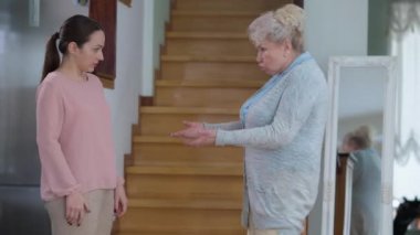 Oturma odasında bağırıp çağırarak konuşan öfkeli genç ve yaşlı kadınların yan görüntüsü. Milenyum yıllarında evde kavga eden emekli ve sinirli insanların orta boy portresi. Nesiller çatışması.