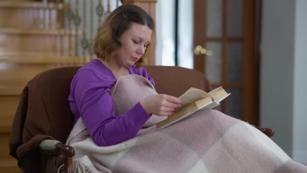 Inteligente mujer caucásica absorbida leyendo libro pensando en un hogar cómodo en el interior. Retrato de mujer inteligente feliz positiva relajada disfrutando de hobby en fin de semana. Inteligencia y estilo de vida. — Vídeos de Stock