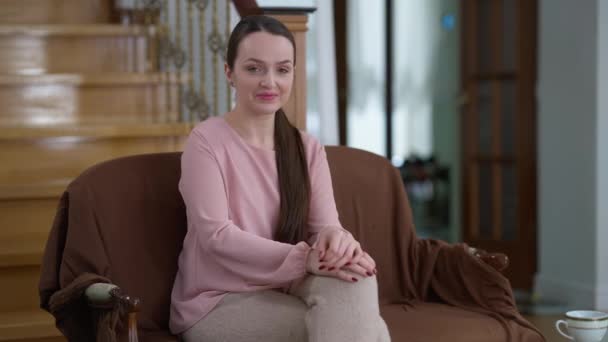 Potret tembakan menengah dari wanita muda Kaukasia cantik yang kurus dan percaya diri yang duduk di kursi yang nyaman di rumah sambil tersenyum mengirimkan ciuman udara ke kamera. Happy Millennial wanita berpose di dalam ruangan — Stok Video