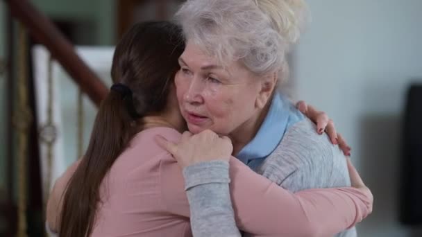 Retrato de la abuela mayor caucásica feliz abrazando a la nieta milenaria hablando acariciando el cabello. Feliz jubilada emocionada disfrutando de la reunión con su nieto en casa dentro. — Vídeo de stock